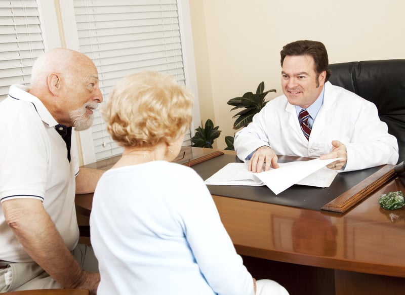 Doctor sitting across a desk from a senior couple gives them good news