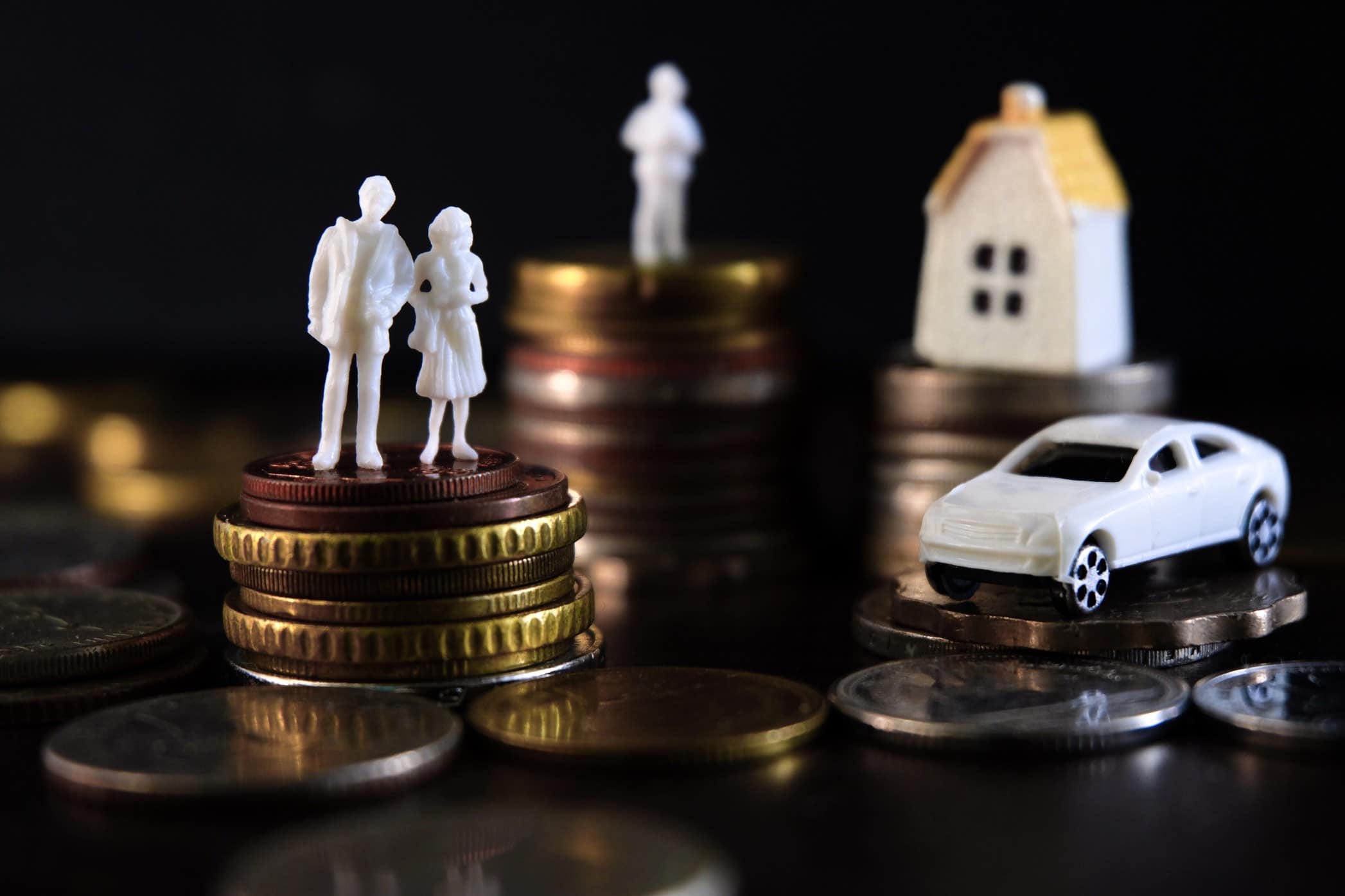 Coins stacked with house sculpture and model car on top with black background